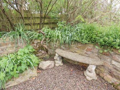 A garden corner with a stone bench gravel ground a metal bird sculpture and plants at Adderstone Cottage in Bamburgh