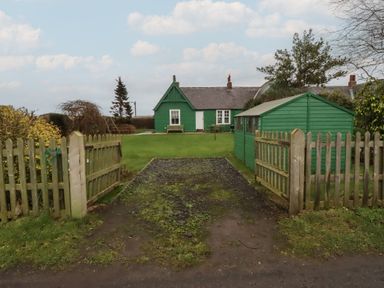 A garden with a green house and fence at Armstrong Cottages No6 in Bamburgh