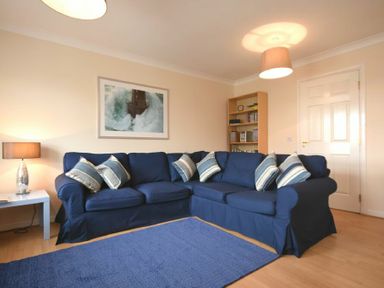 A living room with a blue sectional sofa with striped pillows and a blue rug at Beachcomber Apartment in Bamburgh