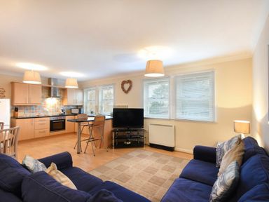 An open-plan living room and kitchen with blue sofas a television and a dining table at Beachcomber Apartment in Bamburgh