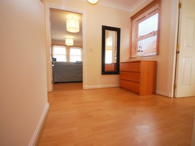 A hallway with wooden floor a chest of drawers and a tall mirror at Beachcomber Apartment in Bamburgh