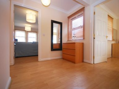 A hallway with a wooden dresser a black framed mirror and windows with wooden blinds at Beachcomber Apartment in Bamburgh