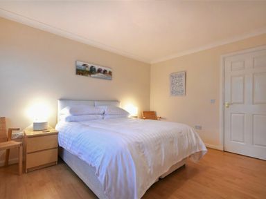 A bedroom with a double bed a nightstand with a lamp two chairs and paintings on the walls at Beachcomber Apartment in Bamburgh