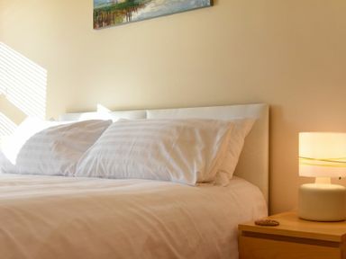 A bed with white pillows and a lamp on a wooden nightstand at Beachcomber Apartment in Bamburgh