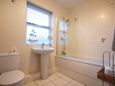 A bathroom with a toilet sink bathtub and a window with blinds at Beachcomber Apartment Bamburgh