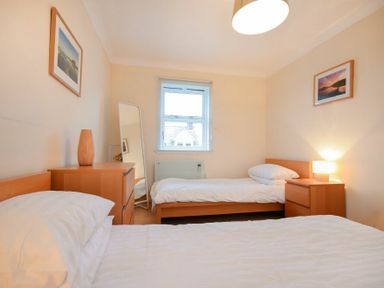 A bedroom with two single beds a dresser a nightstand with a lamp a standing mirror and framed pictures on walls at Beachcomber Apartment in Bamburgh