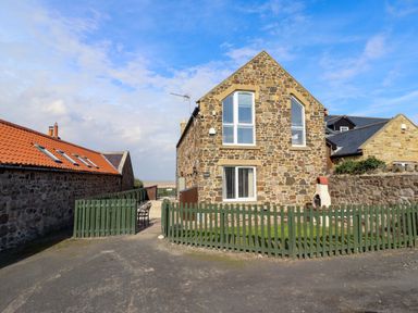 A house with a stone exterior and fenced yard at Pipistrelle in Bamburgh