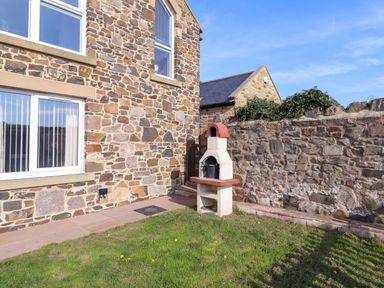 An outdoor area with a stone wall and a barbecue at Pipistrelle in Bamburgh