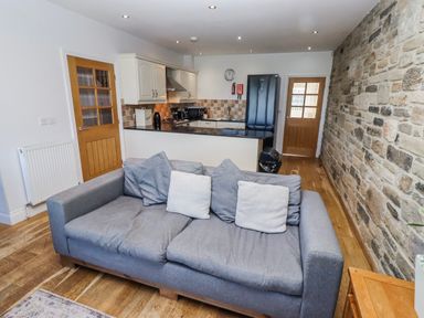 A living room with a sofa and kitchen area at Goosander in Bamburgh