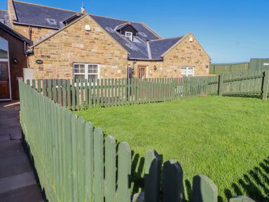 A stone house with a fenced yard at Jackdaw in Bamburgh