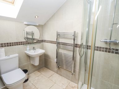 A bathroom with a shower, sink, toilet, and towel radiator at Jackdaw in Bamburgh