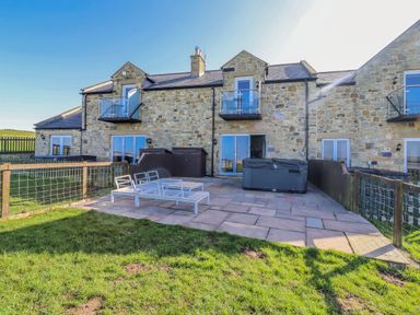 An outdoor patio with a hot tub and seating area at Jackdaw in Bamburgh