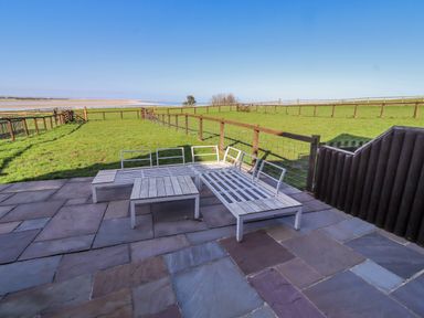 An outdoor patio area with lounge chairs overlooking a grassy field at Jackdaw in Bamburgh