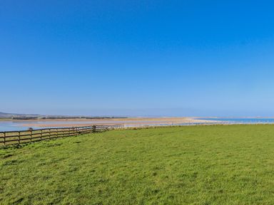 A grassy area with a fence and water under a clear blue sky at Jackdaw in Bamburgh