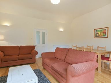 A living room with two red sofas a white coffee table a wooden dining table with chairs and a framed picture on the wall at Decked Out in Alnmouth