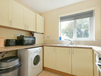 A kitchen with washing machine toaster microwave sink and cabinets at Decked Out in Alnmouth