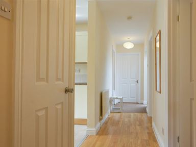 A hallway with wooden floor a radiator a small table and doors at Decked Out in Alnmouth