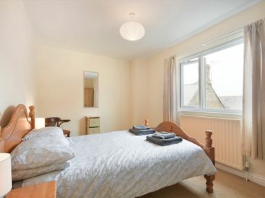 A bedroom with a double bed folded towels on the bed a window curtains a chair a mirror and a small drawer unit at Decked Out in Alnmouth