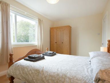 A bedroom with a wooden bed, folded towels, a wooden wardrobe, and a window with curtains at Decked Out in Alnmouth