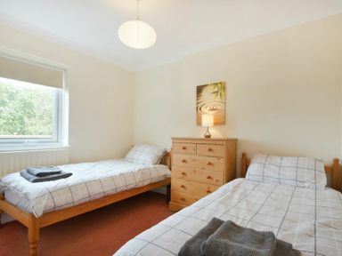 A bedroom with two single beds a wooden chest of drawers and a window at Decked Out in Alnmouth