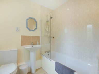 A bathroom with a toilet sink mirror bathtub and shower at Decked Out in Alnmouth
