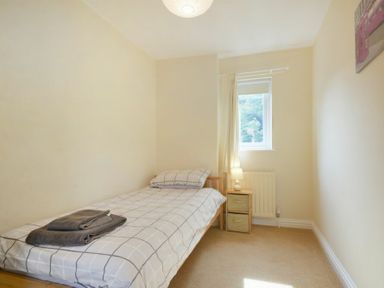 A small bedroom with a single bed a bedside table with a lamp and a window at Decked Out in Alnmouth