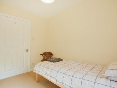 A bedroom with a single bed covered with a checkered duvet and a wooden chair in the corner at Decked Out in Alnmouth