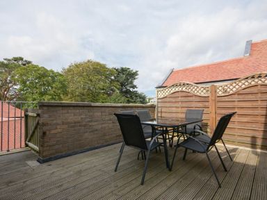 An outdoor patio with a glass table and four black chairs surrounded by a brick wall and wooden fencing at Decked Out in Alnmouth