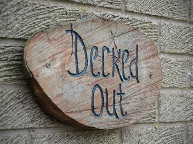 A wooden sign carved with the words Decked Out mounted on a textured stone wall at Decked Out in Alnmouth