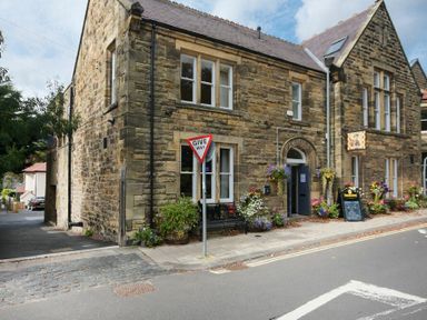 A stone building with windows and an entrance labeled club next to a give way sign and flower pots at Decked Out in Alnmouth