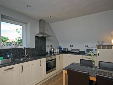 A kitchen with cream cabinets black countertops a window a stove a microwave and a table with chairs at Quarry Mews in Bamburgh