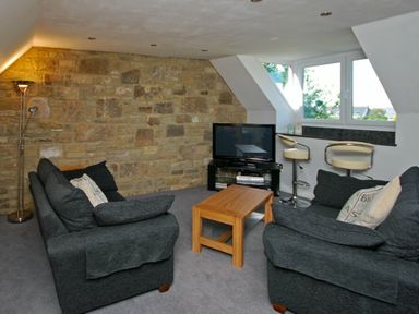 A living room with two sofas a wooden coffee table a television and two bar stools at Quarry Mews in Bamburgh