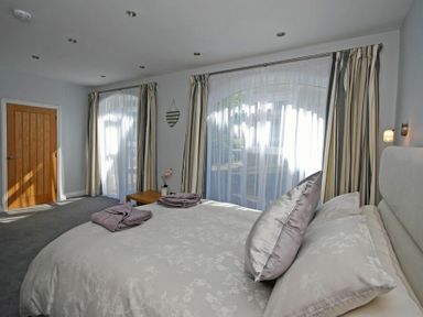 A bedroom with a bed pillows towels on it large windows with curtains and a wooden door at Quarry Mews in Bamburgh