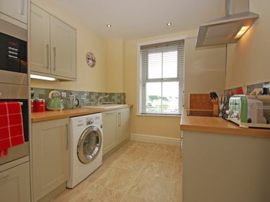 A kitchen with washing machine countertop appliances and window blinds at Coastal Haven in Seahouses