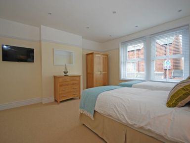 A bedroom with two single beds a wooden chest of drawers a wardrobe and a wall mounted television at Coastal Haven in Seahouses