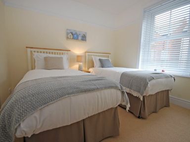 A bedroom with two single beds a nightstand with a lamp and a window with blinds at Coastal Haven in Seahouses