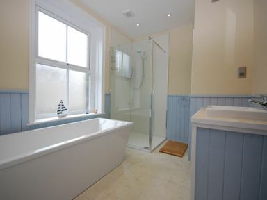 A bathroom with a bathtub shower cubicle sink and window at Coastal Haven in Seahouses