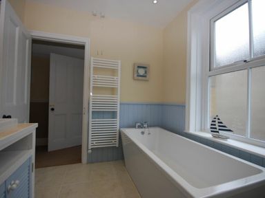 A bathroom with a bathtub towel radiator and window with a model sailboat Coastal Haven Seahouses