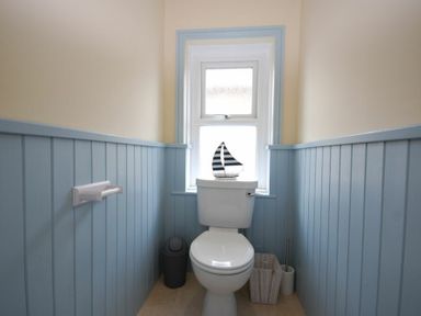 A small bathroom with a toilet a window above and blue wainscoting at Coastal Haven in Seahouses