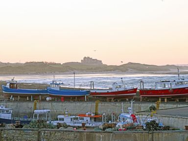 A harbor with fishing boats and nets near the shore with hills and a castle in the distance at Coastal Haven in Seahouses
