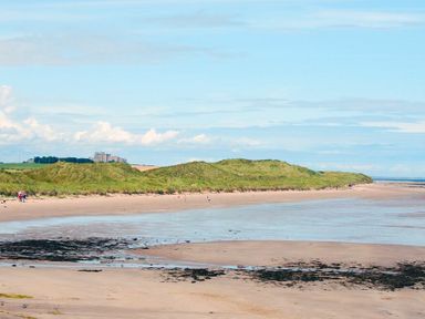 A sandy beach with water and grassy dunes in the background at Coastal Haven in Seahouses
