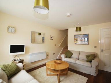 A living room with two sofas a round wooden coffee table and a wall-mounted TV at House Martins Beadnell