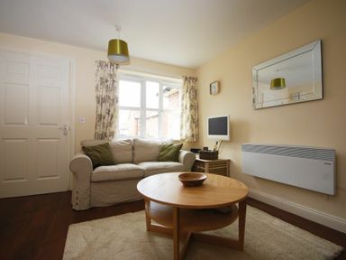 A living room with a sofa green cushions round wooden coffee table and wall-mounted heater at House Martins Beadnell