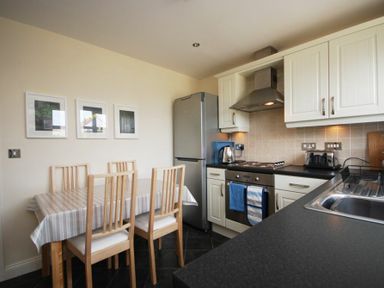 A kitchen with a dining table and chairs next to a fridge oven and sink at House Martins Beadnell