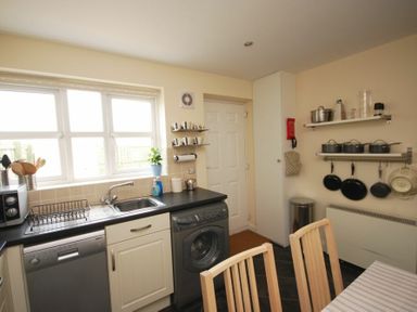 A kitchen with a sink dishwasher washing machine shelves with mugs and pots and pans at House Martins Beadnell