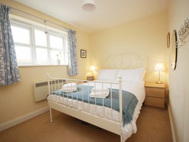 A bedroom with a white metal bed frame blue blanket towels bedside tables with lamps and floral curtains at House Martins Beadnell
