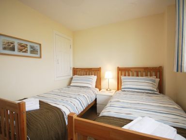 A bedroom with two single beds with striped bedding and a nightstand with a lamp between them at House Martins Beadnell
