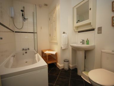 A bathroom with a bathtub shower combination a pedestal sink a toilet a wooden bench and a wall cabinet at House Martins Beadnell