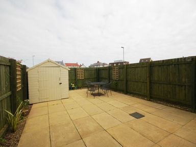 A fenced patio with a shed and a table with chairs at House Martins Beadnell