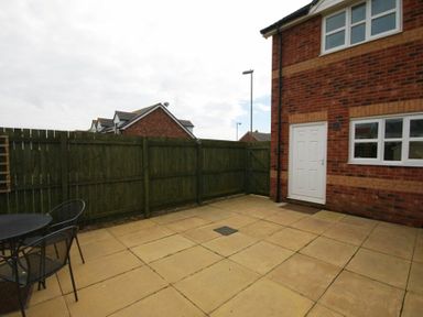 A backyard patio area with square paving stones a wooden fence and a table with chairs at House Martins Beadnell